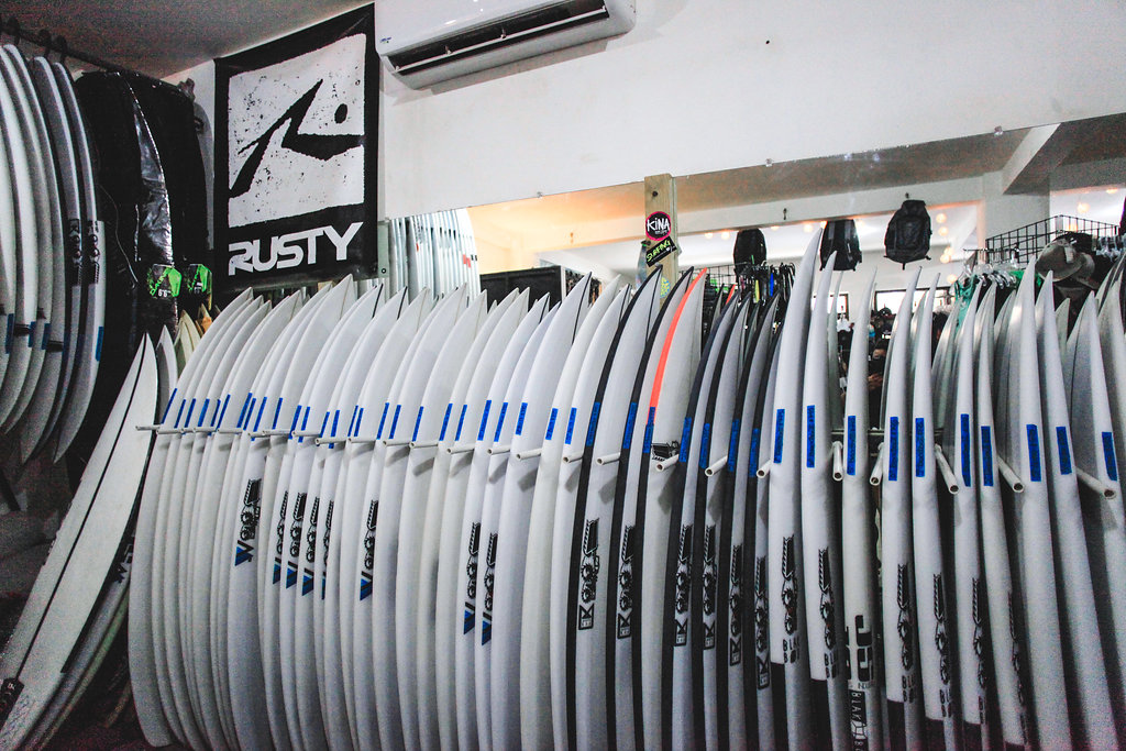 A row of surfboards lined up in a shop with a Rusty flag on the wall.