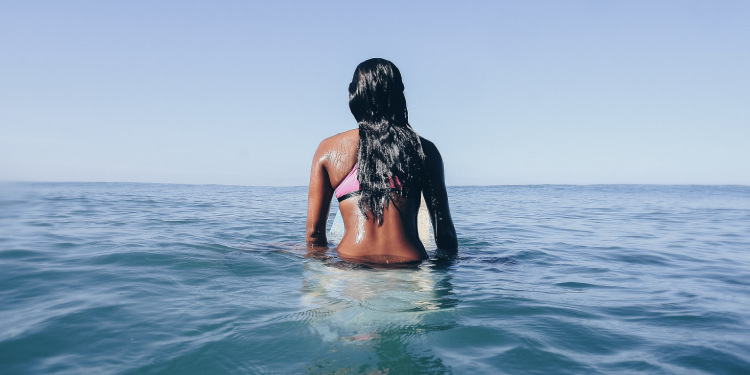Female surfer sitting on surfboard in calm blue ocean near Santa Teresa, Costa Rica, facing horizon in quiet reflection of water conservation.