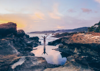 Woman standing between volcanic rock formations at the Santa Teresa coastline, symbolizing water protection and ocean conservation in Costa Rica.