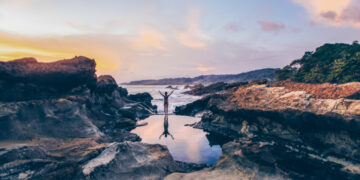 Woman standing between volcanic rock formations at the Santa Teresa coastline, symbolizing water protection and ocean conservation in Costa Rica.