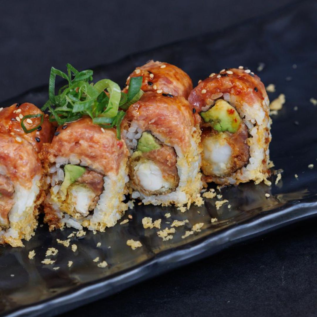 Close-up of sushi rolls with avocado and tempura on a black plate.