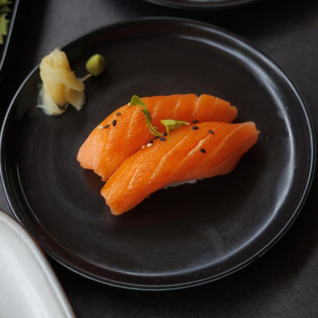 Two pieces of salmon nigiri sushi with wasabi garnish on a black plate.