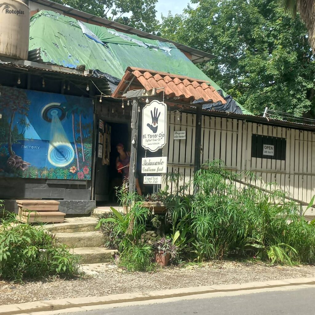 A rustic shop entrance surrounded by greenery on a sunny day.