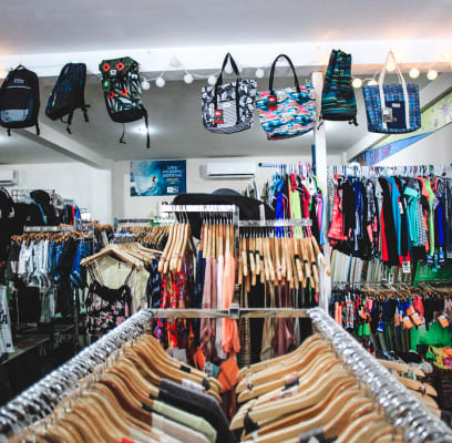 Clothing store interior with racks of colorful clothes and handbags on display.