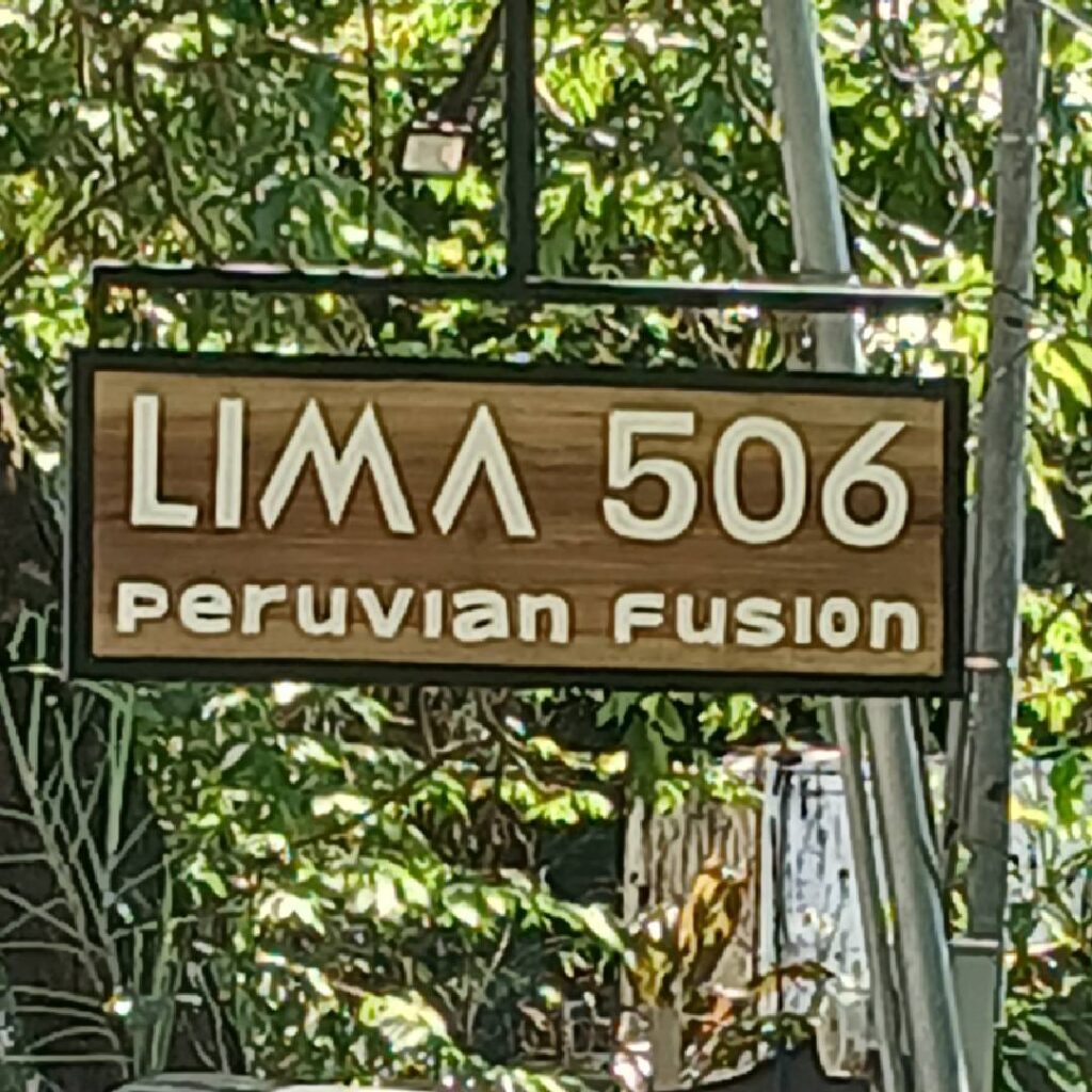 Sign for Lima 506 Peruvian Fusion restaurant surrounded by greenery.