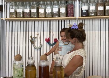 Yuli, clinical herbalist and owner of Marpe Jungle Apothecary, standing with her child at her shop counter surrounded by jars of dried herbs and teas in Santa Teresa Costa Rica