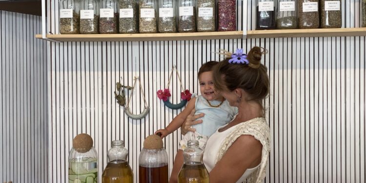 Yuli, clinical herbalist and owner of Marpe Jungle Apothecary, standing with her child at her shop counter surrounded by jars of dried herbs and teas in Santa Teresa Costa Rica