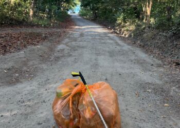 Two orange garbage bags and a trash grabber left on a clean tropical road in Malpaís–Santa Teresa Costa Rica after surfer Bill Dolhancey’s daily trash cleanup walk.