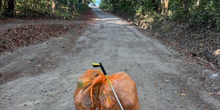 Two orange garbage bags and a trash grabber left on a clean tropical road in Malpaís–Santa Teresa Costa Rica after surfer Bill Dolhancey’s daily trash cleanup walk.