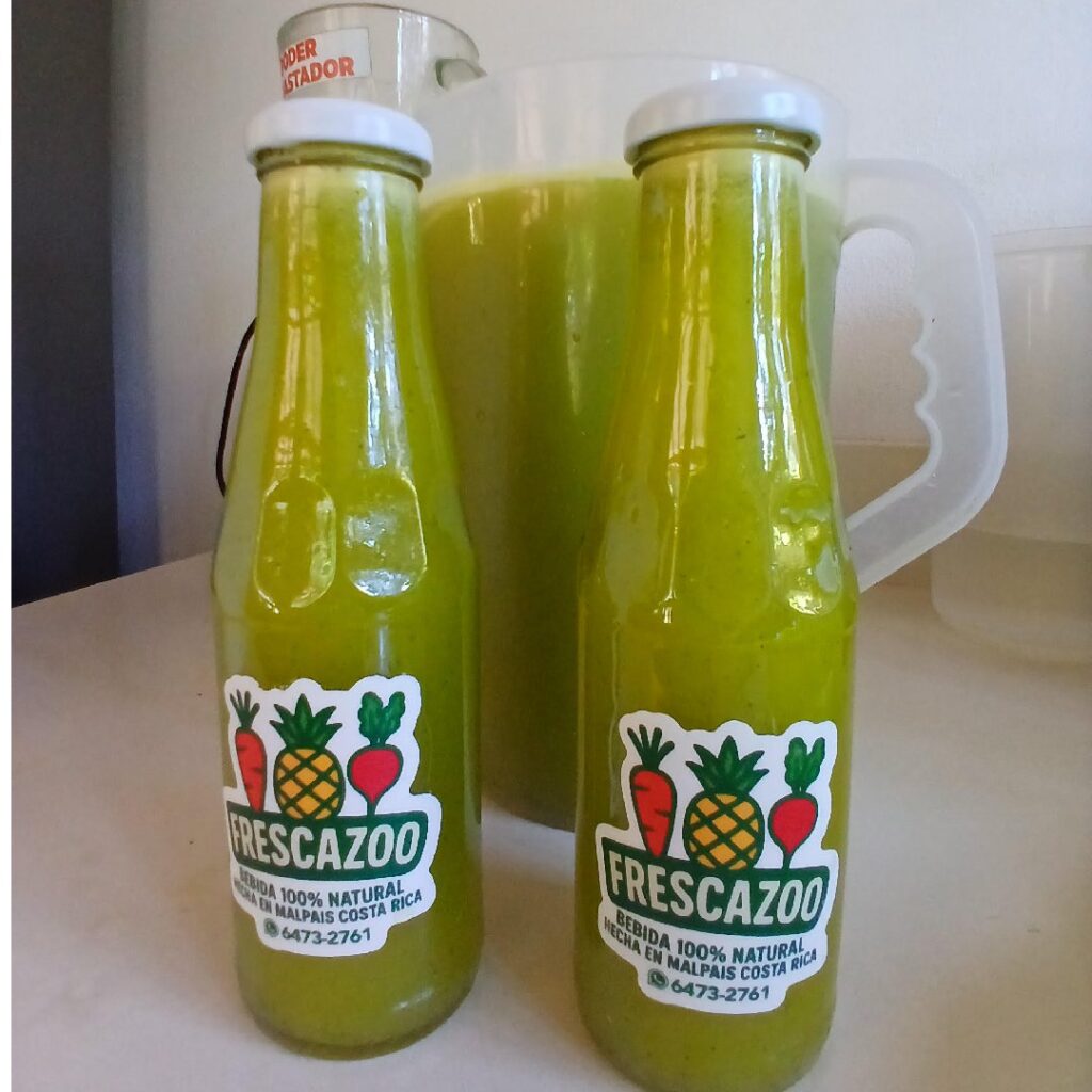 Two glass bottles of Frescazoo juice beside a fresh container of pineapple basil juice in Santa Teresa Costa Rica showing small batch natural juice production made with local ingredients.