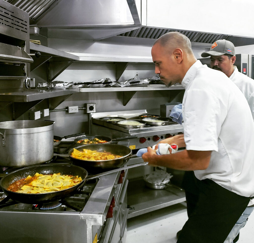 Chef Eitan cooking with flames in kitchen while assistant learns