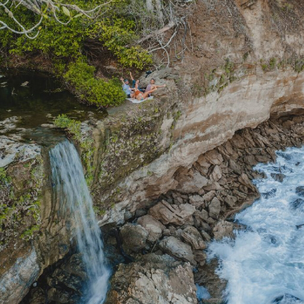 Waterfall flowing over coastal rock with people waving from above Costa Rica