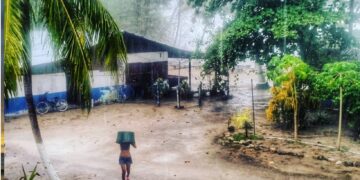 Woman walking through heavy rain in Mal País, Costa Rica, using a bucket for shelter during a tropical rainy season storm near Mar Azul.