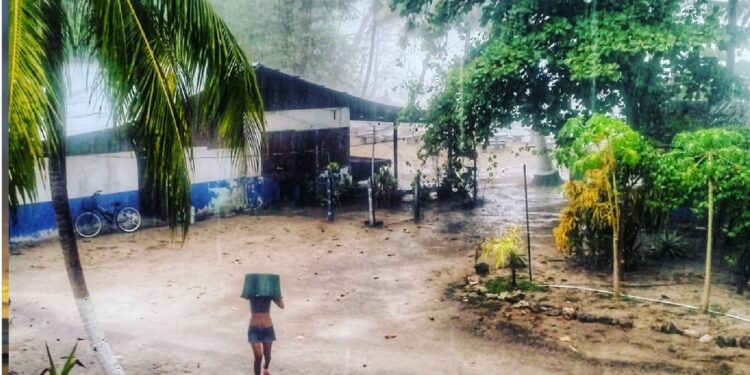 Woman walking through heavy rain in Mal País, Costa Rica, using a bucket for shelter during a tropical rainy season storm near Mar Azul.
