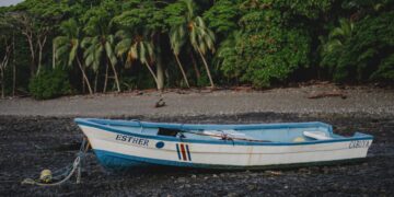 Traditional fishing boat tied at low tide in Malpaís, Costa Rica, with raw jungle coastline and rustic shoreline reflecting the untouched beauty of the 1970s.