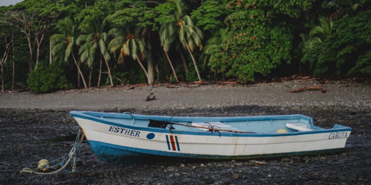 Traditional fishing boat tied at low tide in Malpaís, Costa Rica, with raw jungle coastline and rustic shoreline reflecting the untouched beauty of the 1970s.