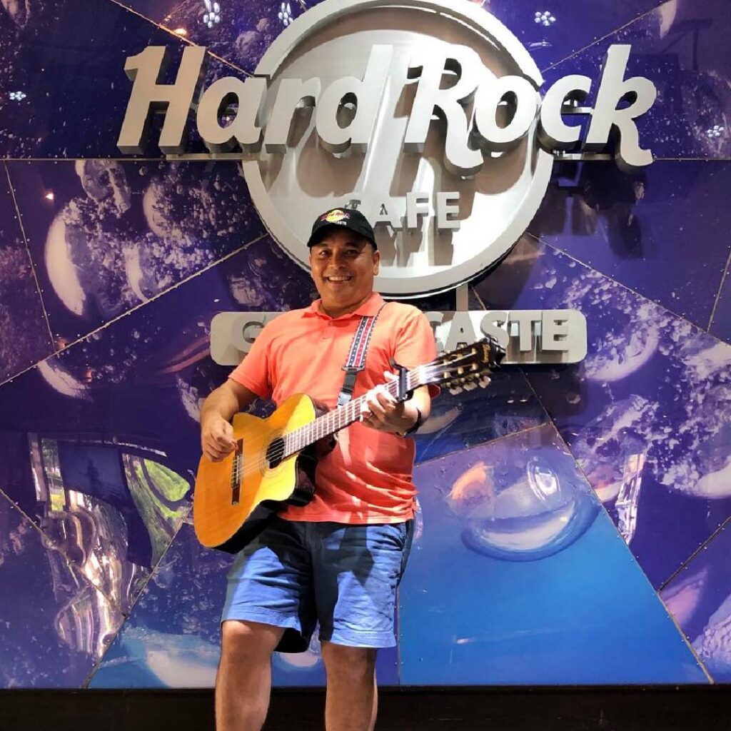 Alan holding a guitar in front of the Hard Rock Cafe sign in Guanacaste, Costa Rica.