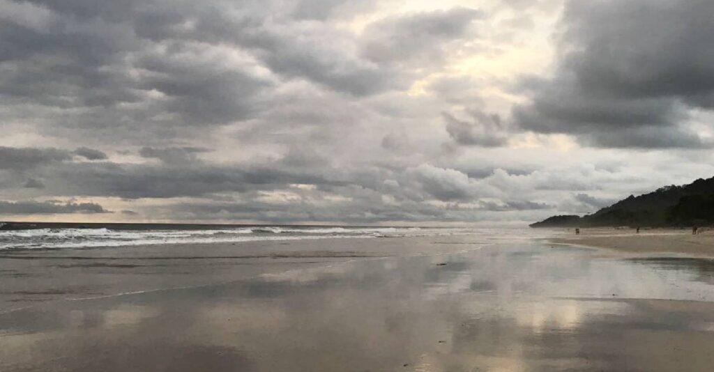 Heavy storm clouds gathering over the Pacific Ocean with reflections in wet sand during low tide in Costa Rica.