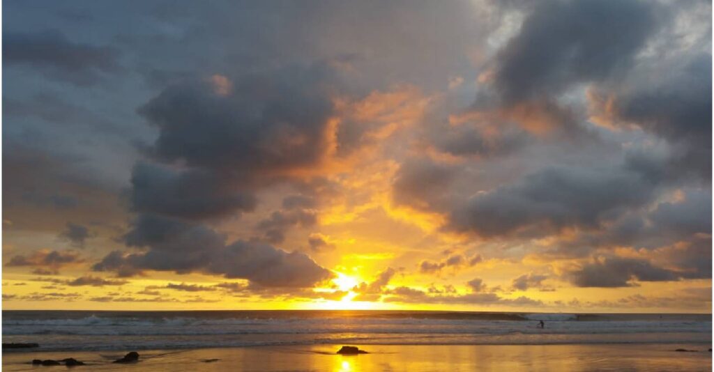 Golden sunset light shining through opening storm clouds over the Pacific Ocean in Costa Rica.